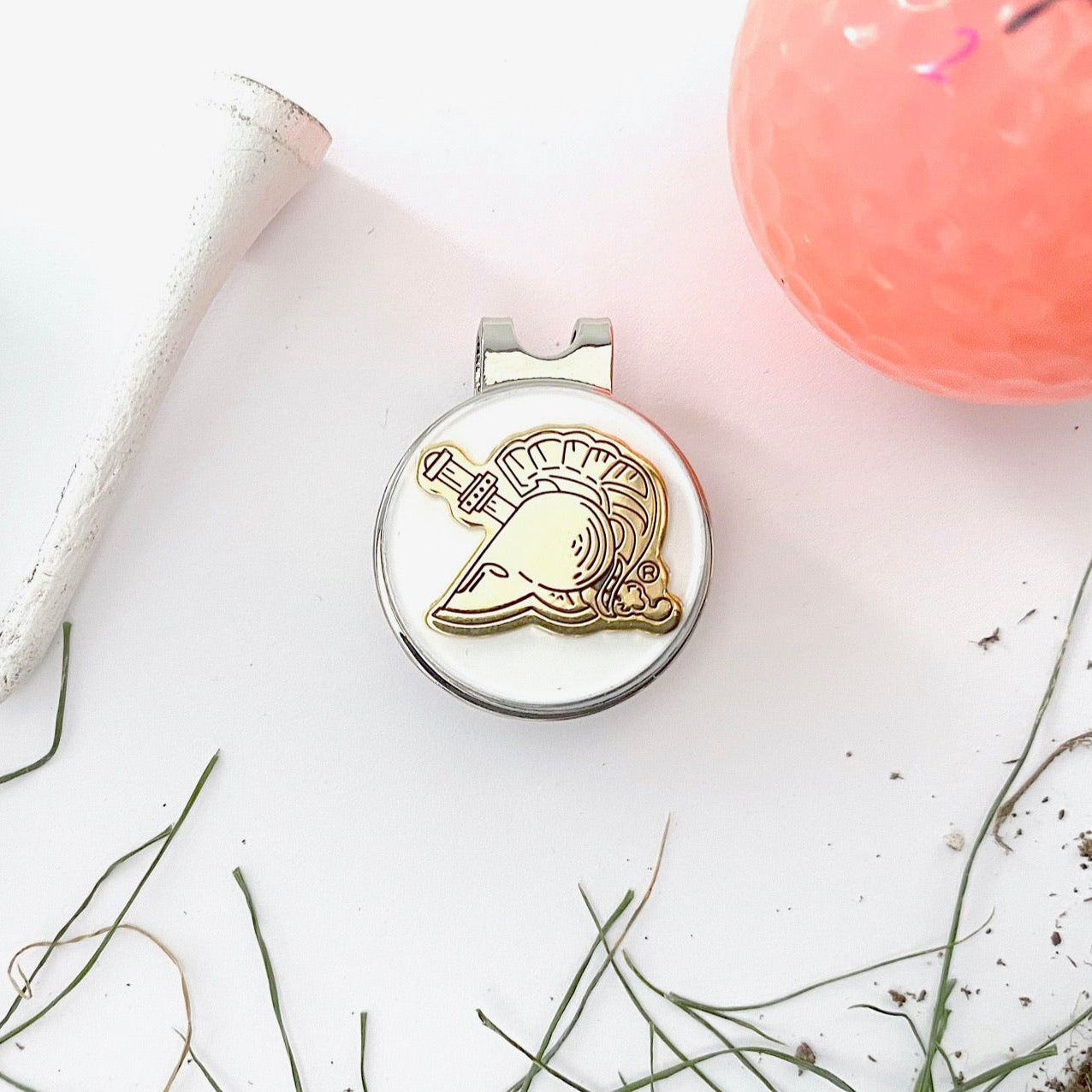 Golf ball marker with dolphin design on a white surface with grass and a pink golf ball.