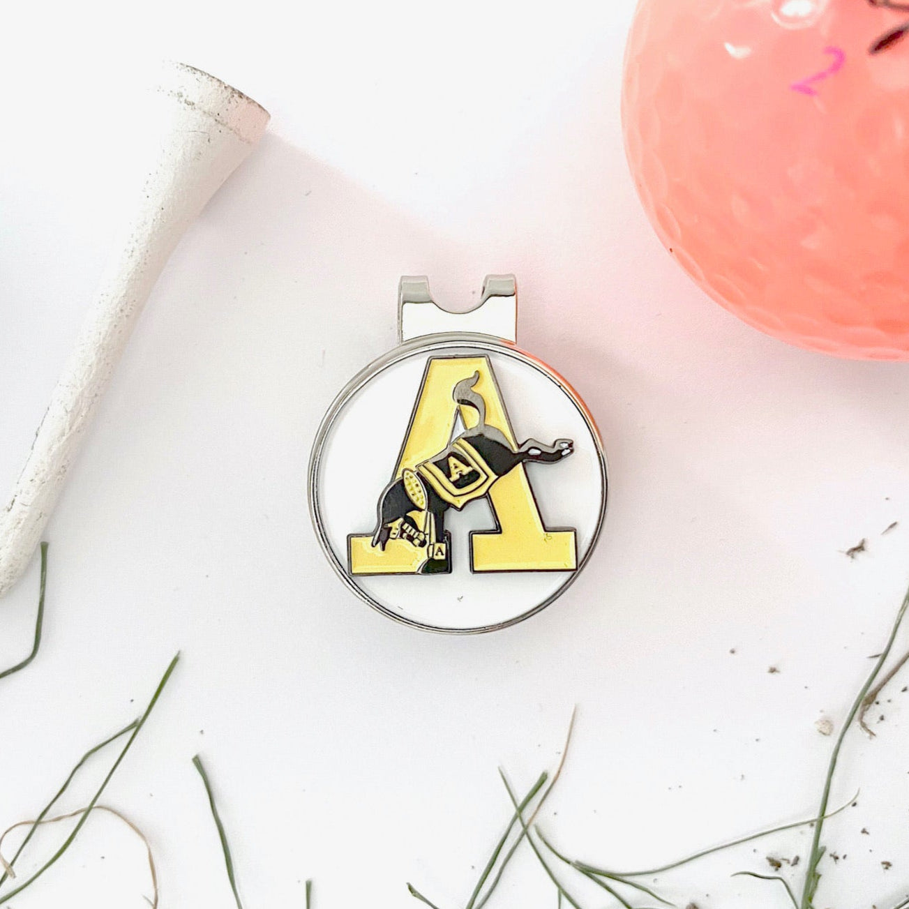 Metallic cap clip with 'A' logo on a white surface