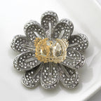 A silver-toned flower-shaped brooch with clear rhinestone detailing, photographed on a white surface.