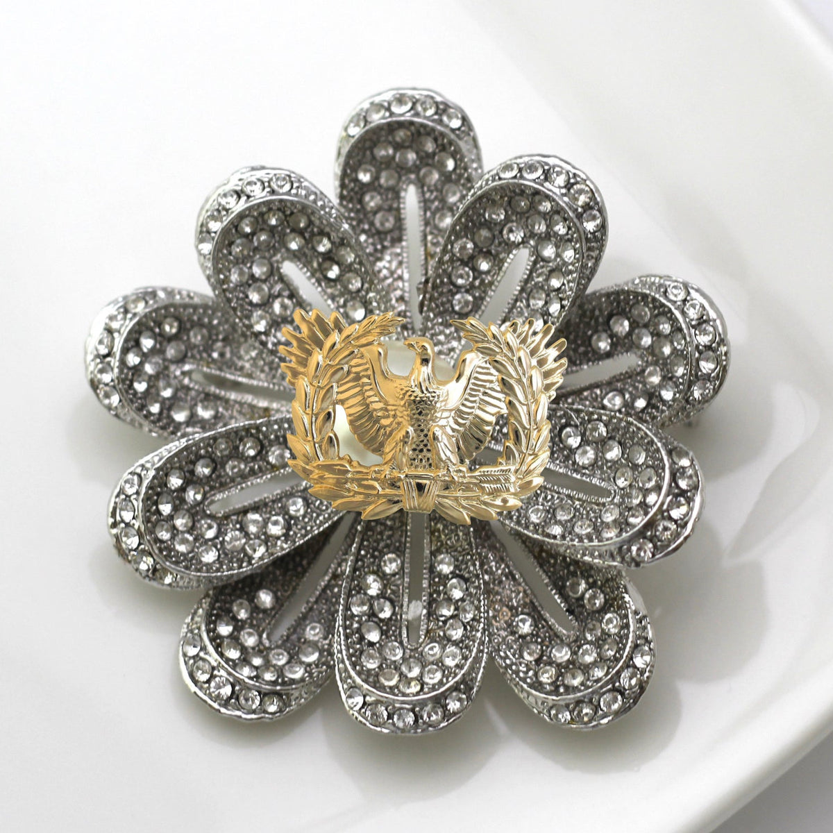 A silver-toned flower-shaped brooch with clear rhinestone detailing, photographed on a white surface.