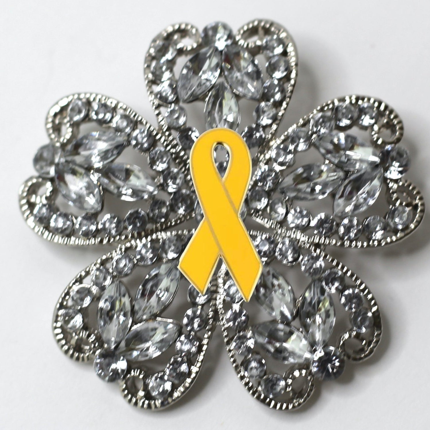 Decorative brooch with a yellow ribbon and crystal-like design on a white background